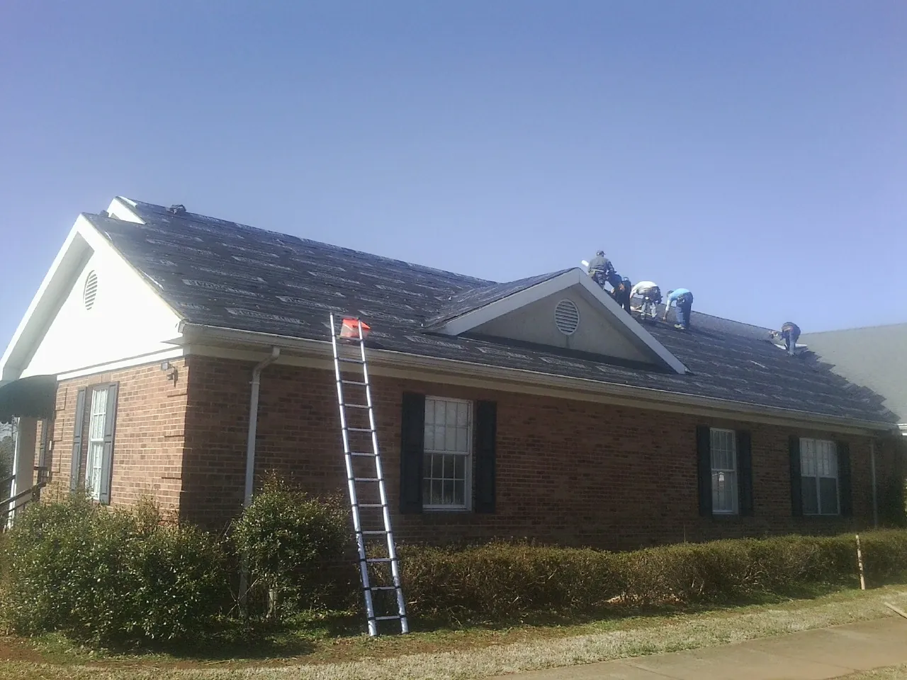 Crew tearing shingles off a brick ranch roof with a ladder set — Emergency Roof Repair work by our crew in Lenox Dale