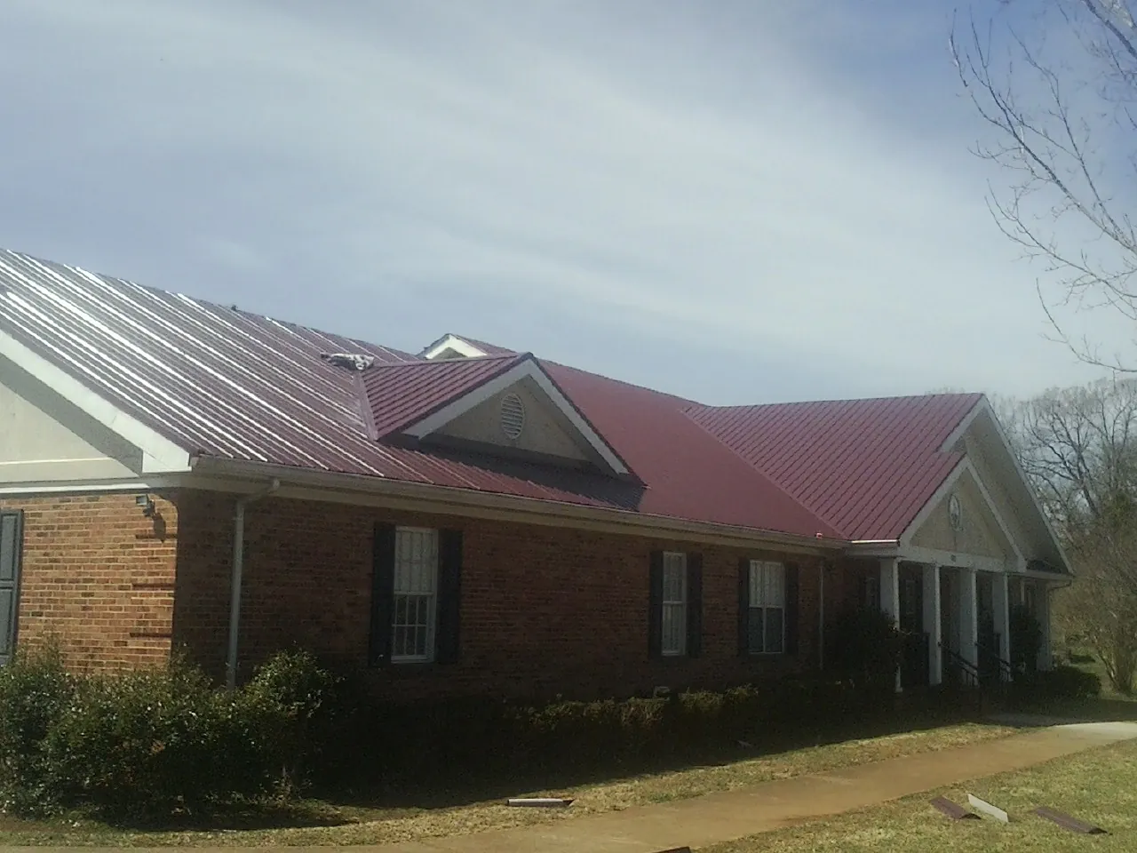 Red metal roof with gabled entries on a long brick building, from a Hail Damage Roof Repair job in Lenox Dale