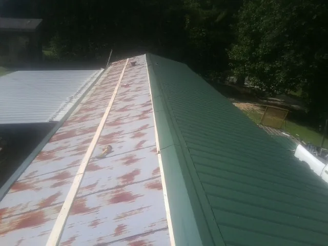 Old rusted panels beside newly installed green metal roofing — Wind Damage Roof Repair by Roofing Brothers in Lenox Dale