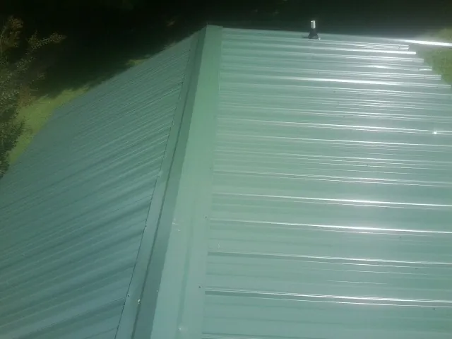 New green metal panels meeting at the ridge of a roof — Flat Roof Repair work by our crew in Lenox Dale