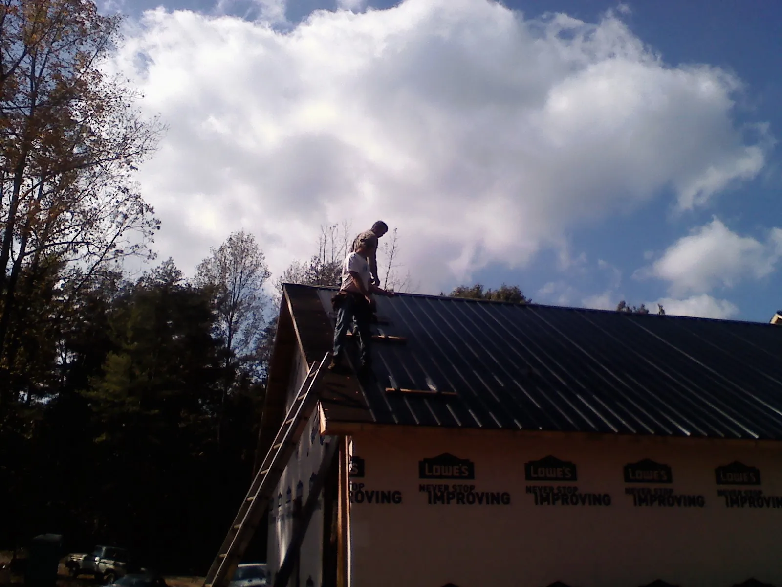 Roofer fastening dark metal panels high against a cloudy sky, from a Roof Inspection job in Lenox Dale