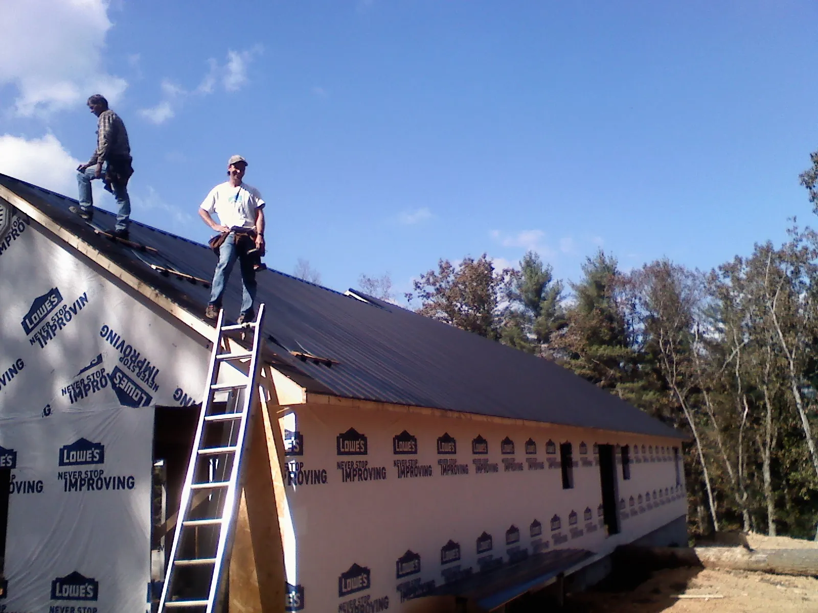 Two roofers standing on a long dark metal roof over a wrapped building in Lenox Dale