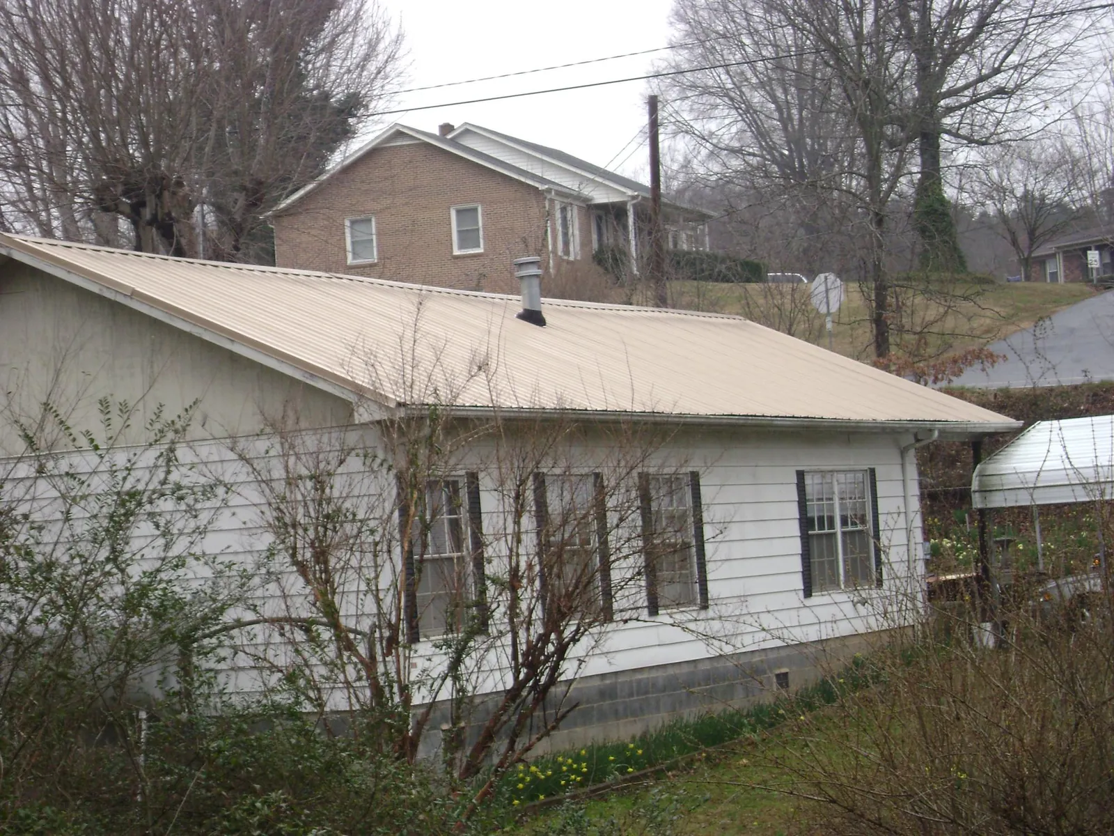 Tan metal roof on a white sided house set into a hillside — Commercial Roofing by Roofing Brothers in Lenox Dale
