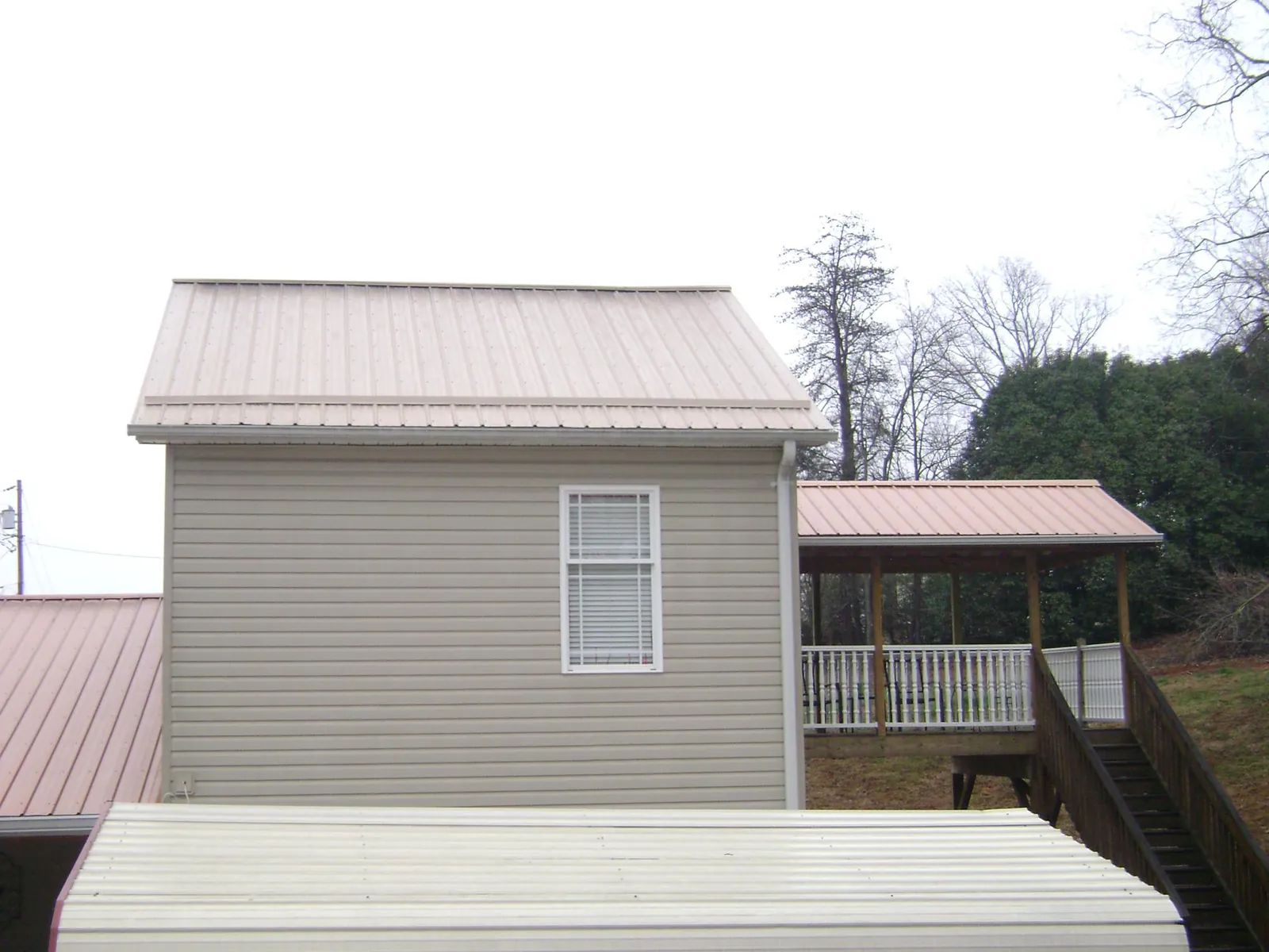 Tan metal roofs on a two story addition and attached porch, from a Roof Replacement job in Lenox Dale